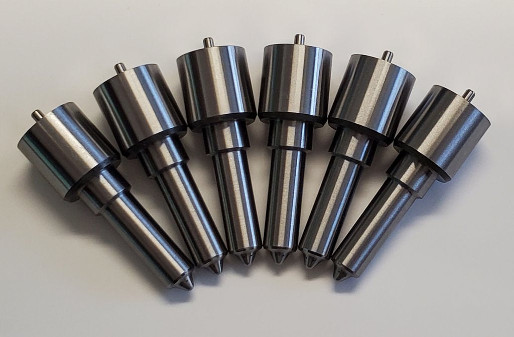 Eight Cummins VE Pump Stage 1 nozzle sets from Dynomite Diesel with conical shapes lined up symmetrically on a light surface.